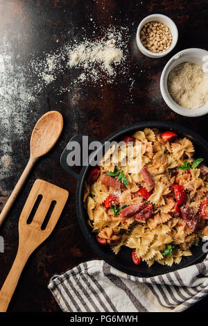 view from above of pasta with jamon, pine nuts, sauce, cherry tomatoes, mint leaves covered by grated parmesan in pan surrounded by kitchen towel, woo Stock Photo
