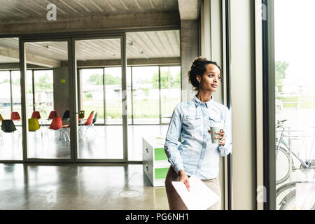 Confident young businesswoman leaning on window in modern office Stock Photo