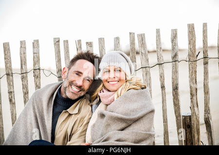 Portrait of smiling couple wrapped in blanket on the beach Stock Photo