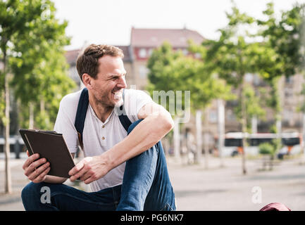 Smiling man sitting outdoors with tablet Stock Photo