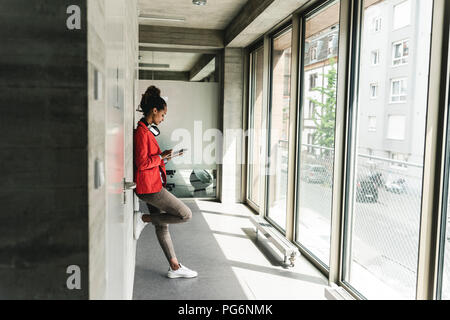 Young woman with headphones standing in corridor, using digital tablet Stock Photo