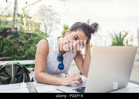 Portrait of laughing young woman using laptop outdoors Stock Photo