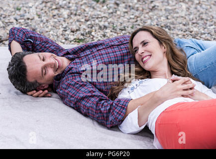 Happy affectionate couple lying on a blanket at pebble beach Stock Photo