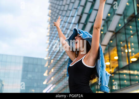 Carefree young woman wearing black dress in the city at dusk Stock Photo