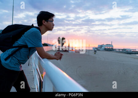 Young Chinese man with backpack looking at beach Stock Photo