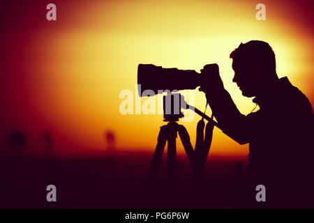 Golden Hour Photography. Silhouette of Men Taking Pictures with Large Telephoto Lens. Stock Photo