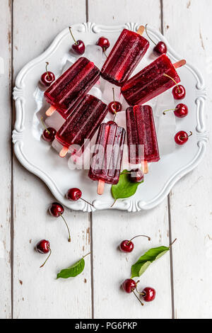 Homemade cherry ice lollies, ice cubes and cherries on plate Stock Photo