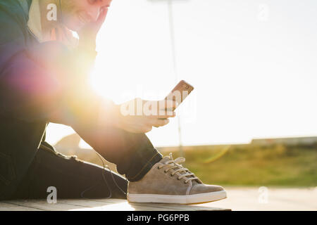 Man with headphones sitting on wood stack, using smartphone Stock Photo