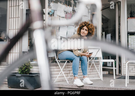 Woman in front of coffee shop, holding smart phone Stock Photo