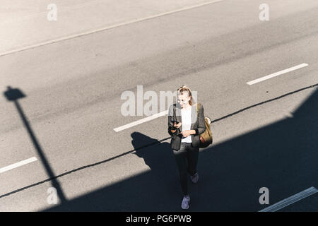 Young woman walking on empty road, talking into her smartphone Stock Photo