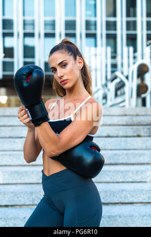 Portrait of sportive young woman putting on boxing gloves in the city