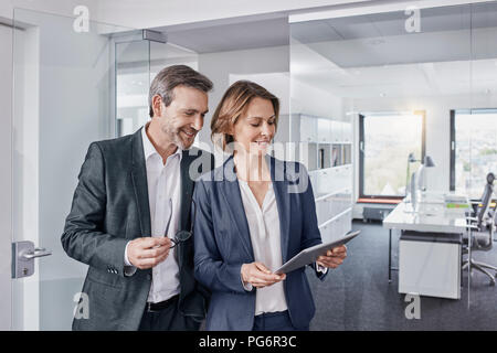 Smiling businessman and businesswoman using tablet in office together Stock Photo