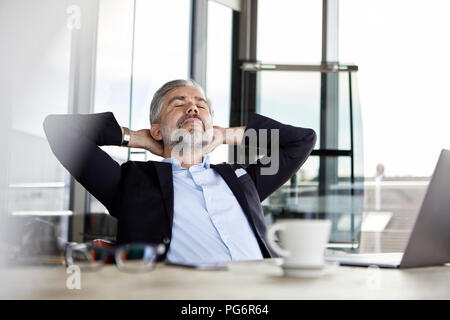 Businessman at desk in office leaning back Stock Photo