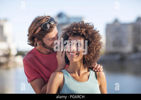Happy young couple, man whispering into woman's ear Stock Photo