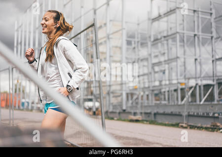 Happy sportive young woman standing at hoarding Stock Photo