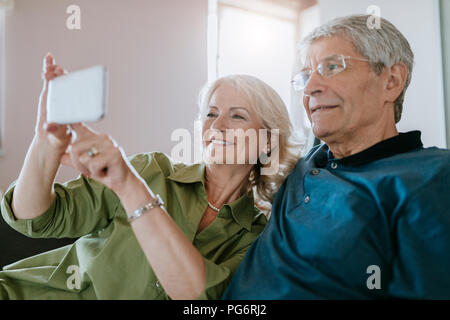 Senior couple at home sitting on couch taking a selfie Stock Photo
