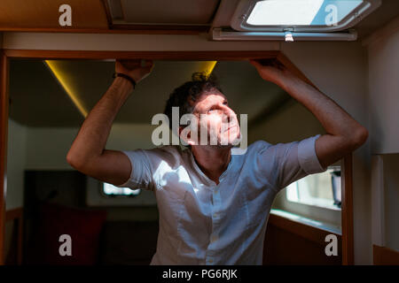 Mature man standing in catamaran cabin, looking up through hatch Stock Photo