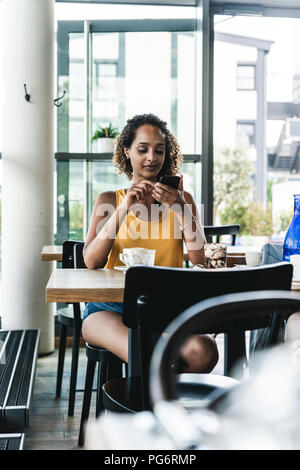 Young woman sitting in cafe, drinking coffee, reading text messages Stock Photo