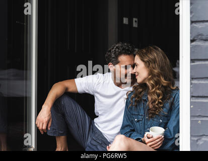 Affectionate couple in nightwear at home sitting at French window Stock Photo