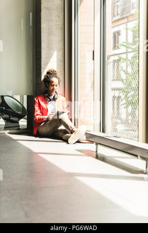 Young woman with headphones sitting on floor, using digital tablet Stock Photo