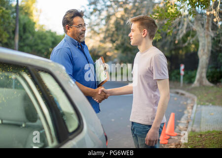 Learner driver and instructor shaking hands at car Stock Photo