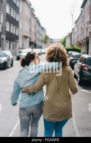 Best friends walking in the city, arm in arm, rear view