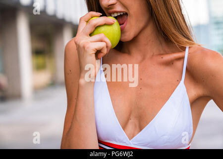 Close-up of young woman wearing sports bra eating an apple Stock Photo