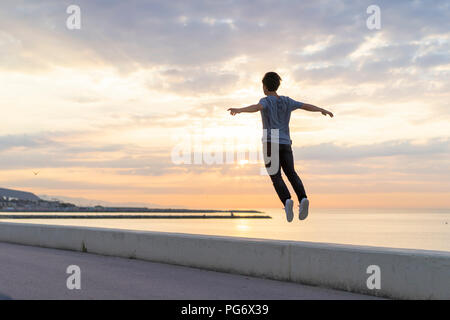 Young Chinese man jumping on wall at the beach Stock Photo