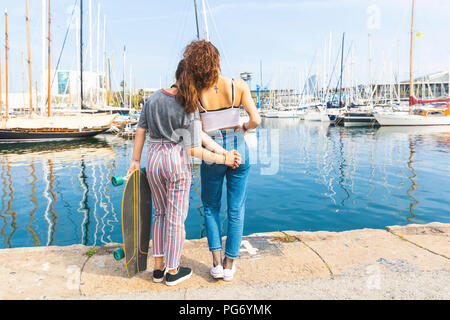 Young woman and teenage girl with a skateboard standing at marina Stock Photo