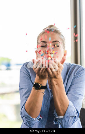 Happy businesswoman blowing confetti, celebrating success Stock Photo