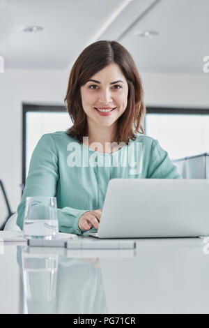 Portrait of smiling young businesswoman using laptop at desk in office Stock Photo