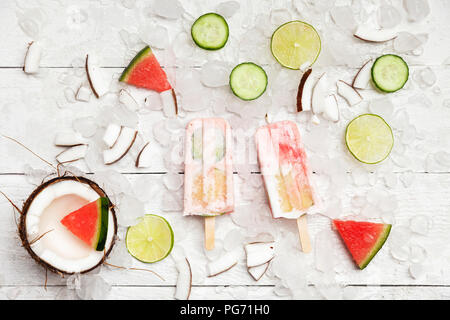 Homemade watermelon coconut ice lollies with lime and cucumber slices, fresh coconut and watermelon pieces on ice cubes Stock Photo