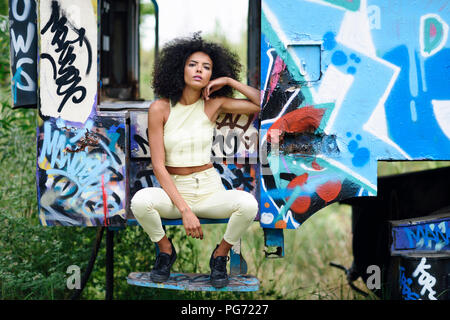 Portrait of fashionable young woman sitting on steps of an abandoned and destroyed old train Stock Photo