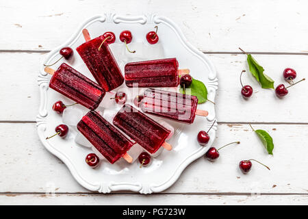 Homemade cherry ice lollies, ice cubes and cherries on plate Stock Photo