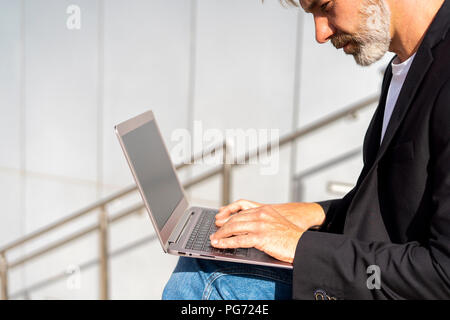 Businessman sitting outdoors using laptop Stock Photo