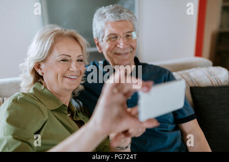 Senior couple at home sitting on couch taking a selfie Stock Photo