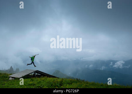 Germany, Brauneck, young hiker with hiking poles and backpack jumping in the air Stock Photo