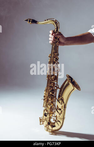 close-up partial view of man holding saxophone in smoke on grey Stock Photo