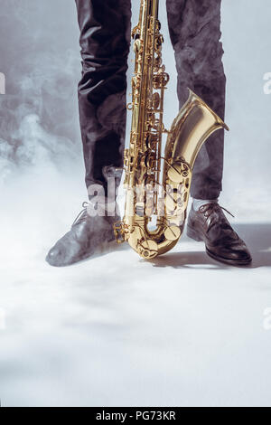 partial view of young musician standing with saxophone in smoke on grey Stock Photo