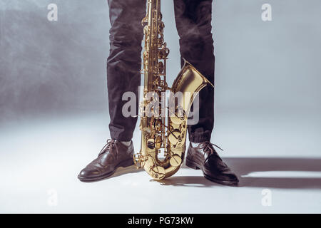 partial view of professional musician standing with saxophone in smoke on grey Stock Photo