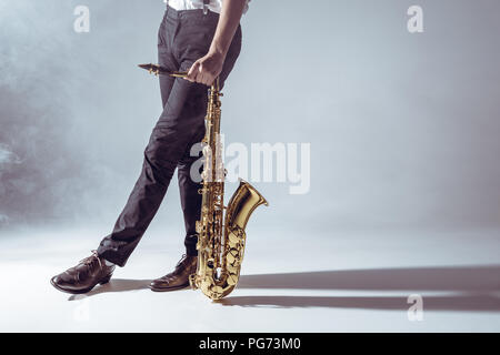 cropped shot of professional musician standing with saxophone in smoke on grey Stock Photo