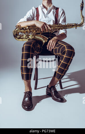 cropped shot of stylish professional musician sitting with saxophone on grey Stock Photo