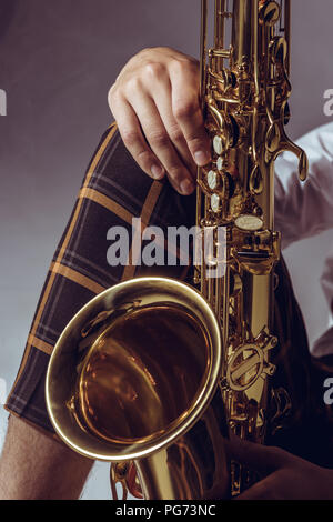 close-up partial view of stylish professional musician holding saxophone on grey Stock Photo