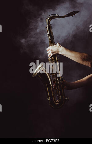 cropped shot of musician holding saxophone in smoke on black Stock Photo