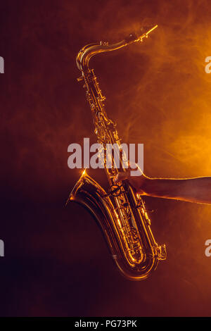 close-up partial view of young musician holding saxophone in smoke Stock Photo