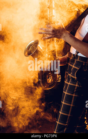 cropped shot of expressive young musician playing saxophone in smoke Stock Photo