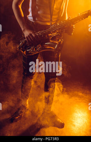 low section of young musician holding saxophone in smoke Stock Photo