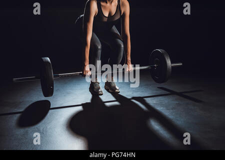 partial view of sportswoman exercising with barbell, black background ...