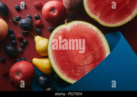 elevated view of ripe fruits and blue paper on red surface Stock Photo