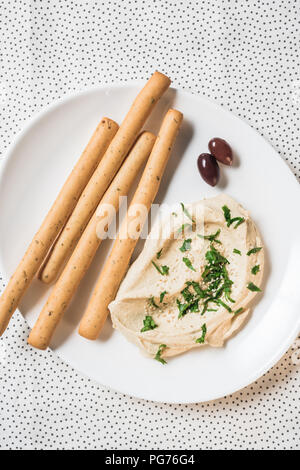 top view of hummus, breadsticks and olives on plate on linen Stock Photo